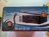 Front of the box showing brand Moukey, model MAMP1 with image of the power amplifier and remote control. Indicates compatibility with MP3, WMA, USB, AUX