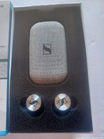 Open box showing the two earbuds and the fabric-textured charging case inside foam cutout.