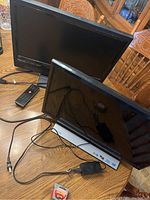 Two flat screen LED TVs displayed on wooden table; Vizio 21-inch in foreground with remote and power adapter, Samsung 23-inch in background with remote adjacent.
