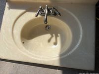 Top view of an ivory-colored bathroom sink with oval basin, faucet handles and spout attached. Visible dirt and wear marks.