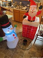 Wide view showing both inflatable decorations and the tree stand on floor near kitchen area.