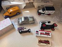 Six diecast vehicles including two coin banks with original boxes, displayed on table.