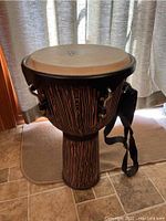 Full view of the djembe drum showing wooden carved body and attached carrying strap.