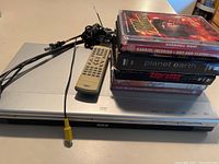 Photo of silver RCA DVD player with remote control and AV cables on top