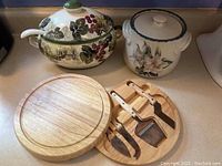 Ceramic soup tureen with grapevine design, ceramic oven-proof crock with floral pattern, wooden swivel cheese board with cheese knives displayed