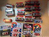 Multiple boxed and blister-packaged Matchbox NASCAR and racing cars laid out on a wooden surface. Various designs including Tide Racing Team and others visible.
