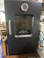 Front view of black vertical cabinet smoker with glass door, stainless steel handle and built-in analog thermometer.