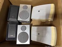 3 pairs of speakers in a cardboard box: black Optimus, white Yamaha outdoor, and white JMC speakers
