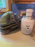 Jack LaLanne Power Juicer and Bissell SpotBot pet carpet cleaner placed side by side on a counter.