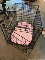 Black metal wire small dog crate containing a used pink cushioned dog bed; view from the front door