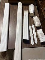 Photo of multiple white vinyl straight spouting pieces showing fluted design along with 4 corner connectors and 2 decorative/support pieces arranged on wooden floor