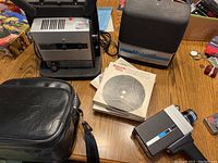 Overview of the Super 8 movie camera, projector, case, and manuals displayed on a table.