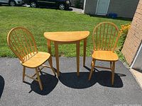 Full set of half-circle wooden table and two wooden chairs placed outside on driveway with grass background.