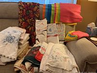 Wide view showing variety of table cloths and fabric items on couches with different colors and patterns including floral embroidery and seasonal prints