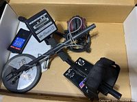 Photo of boxed Whites metal detector showing controller unit, search coil, arm cuff, and cables.