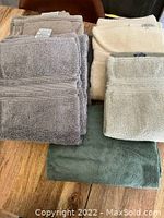 Four stacks of folded towels and napkins showing various colors including grey, beige, cream, and sage green on a wooden table surface.