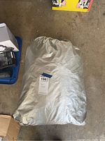 Silver automotive car cover tightly packed inside a matching silver storage bag with a tag marked '198'.