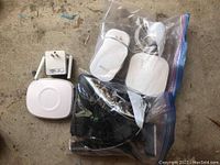 White Eero hub device with power adapter, two additional Eero accessories, and multiple cables in plastic bags on concrete surface
