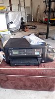 Epson ET-3600 all-in-one printer sitting on a brown cushioned surface with visible screen and control panel.