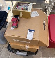 Boxed holiday decorations including a boxed Christmas ornament and stacked cardboard boxes outdoors, some black plastic storage bins visible beneath.