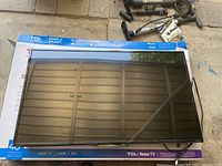 Front view of the 40-inch Insignia TV turned off, laying on top of a TCL box, showing screen and black bezel.