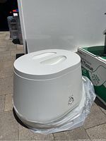 White Lomi composter unit on plastic sheeting showing front dial and hinged lid