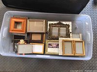 Assortment of various sized photo frames including wood, gold ornate, mosaic tile, and novelty monkey shape in plastic bin