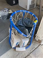 Blue metal framed basketball hoop with white net, two boxes of Leslie's Fresh Clear Chlorine, and black inflatable pump or cover visible on the floor.