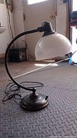 Full view of Pottery Barn desk lamp angled to show curved metal arm and glass shade.