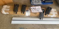 Skybar V2 roof rack components laid out, showing two aluminum crossbars, four black mounting brackets, the original packaging box, and a plastic case with tools or hardware.