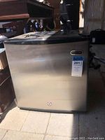 Photo of stainless steel Whynter mini freezer front with black top, lock at bottom center, model and condition tag attached.