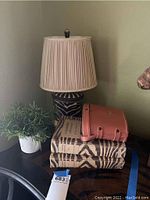 Animal print ceramic table lamp with pleated beige lampshade, stacked animal print books, pink small purse, black binoculars and faux plant on black table.