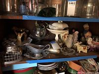 Shelf display showing assortment of ceramic animal figurines, metal serving pieces, and stands.