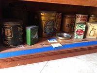 Shelf containing multiple vintage tins arranged in a row, showing front labels and colors.