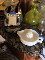 Front view of Proctor streamlined chrome toaster next to white ceramic Sunkist citrus juicer on granite countertop.