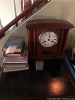 Photo showing the vintage wooden mantel clock next to a stack of vintage books and a small silver box on a dark surface