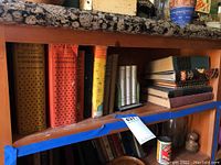 Shelf containing multiple vintage cookbooks with colorful worn covers and various sizes.