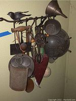 Full view of vintage metal and wood cooking utensils hanging on decorative wall mount with bird figure