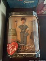 Front view of the doll in original packaging showing the doll in checkered dress and the packaging graphics.