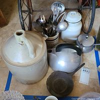 Photo showing entire lot including large stoneware jug, metal teapot, small metal pot, cast iron pan, and assortment of utensils in stoneware crock.