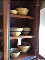 Photo of wooden cabinet shelves holding various vintage mixing bowls in yellow and beige tones, stacked and arranged by size.