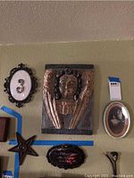 Vintage wall art group including carved angelic plaque, oval plaque with number '3', star ornament, small black plaque with text, oval framed picture of woman with horse, and small ornamental bird figure.