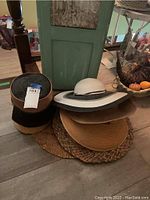 Photo showing multiple vintage women's hats including straw hats with wide brims, gray felt hat, and fabric hats with decorative trims.