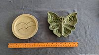 Two ceramic items shown side by side with measuring ruler; round bird dish on left, butterfly dish on right
