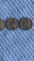 Four silver nickel coins laid out on a blue textured fabric, showing obverse side featuring Thomas Jefferson's profile.