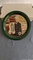 Front view of the round Coca Cola tray with vintage design, placed on gray fabric with a cardboard box behind it.