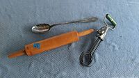 Photo showing wooden rolling pin, metal spoon, and green-handled vintage hand drill laid out on a blue cloth.