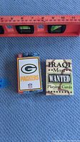 Two decks of playing cards with a measuring level showing approximate size. One deck is Green Bay Packers themed, the other is "Iraqi Most Wanted" camouflage themed.