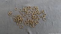 Multiple small to medium gold-tone metal rings spread out on cloth surface