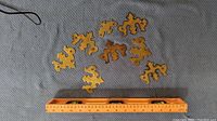 Top-down view of 10 solid brass Colonial Chippendale style decorative hardware pieces arranged on fabric background with measuring ruler for scale.
